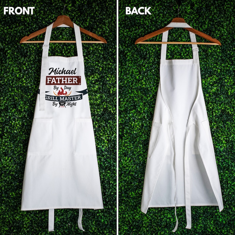 May include: White apron with adjustable straps and a large pocket. The front of the apron has a design that says "Michael Father by Day Grill Master by Night".