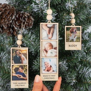 May include: Three wooden photo ornaments with string hangers and wooden beads. The ornaments feature photos of a couple, a baby, and a dog. The ornaments have the text "First Married Christmas", "Noah's First Christmas", and "Buddy".
