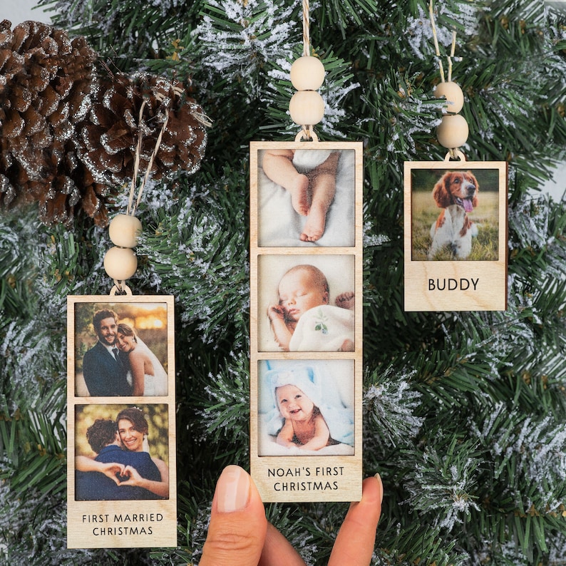 May include: Three wooden photo ornaments with string hangers and wooden beads. The ornaments feature photos of a couple, a baby, and a dog. The ornaments have the text "First Married Christmas", "Noah's First Christmas", and "Buddy".