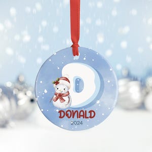 May include: A blue and white Christmas ornament with a snowman and the letter D. The ornament also has the name Donald and the year 2024.