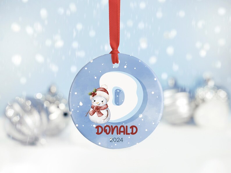 May include: A blue and white Christmas ornament with a snowman and the letter D. The ornament also has the name Donald and the year 2024.