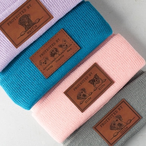 May include: Four different beanie hats with personalized leather patches. Each patch features a dog's photo and name. The hats are in various colors: purple, blue, pink, and gray.