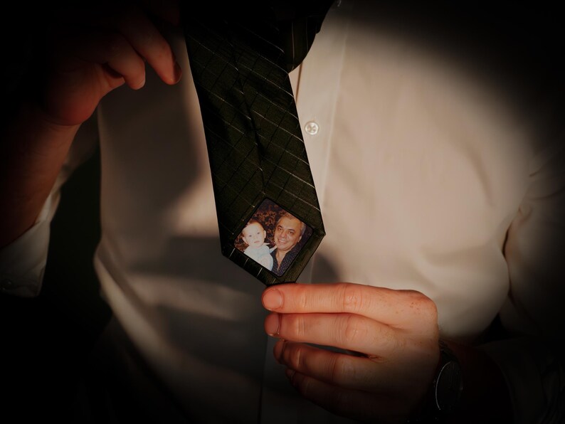 May include: A dark green patterned tie with a small photo of a man and a child inside a clear plastic window.