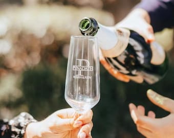 May include: A person pouring champagne into a clear glass champagne flute. The flute is engraved with the text "Pynadath" and "Edwin & Judy".
