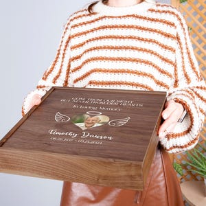 May include: A wooden box with a personalized inscription, "Gone from our sight but never from our hearts, in loving memory, Timothy Dawson 08.26.1917 - 03.15.2024". The box has a heart-shaped cutout with a photo of a person inside.