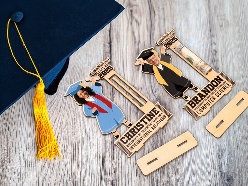 Op de afbeelding: Houten afstudeercadeaus met cartoon afgestudeerden, gepersonaliseerd met namen en universiteitsdetails. De cadeaus bevatten de tekst "Gefeliciteerd! Klas van 2025". Een blauwe afstudeerhoed met een gele kwast is ook zichtbaar.