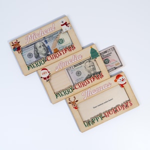 May include: Three wooden Christmas money holders with festive designs. The top holder says "Micheal Merry Christmas" and features a polar bear. The middle holder says "Amelia Merry Christmas" and features Santa Claus. The bottom holder says "Thomas Happy Holidays" and features a snowman.