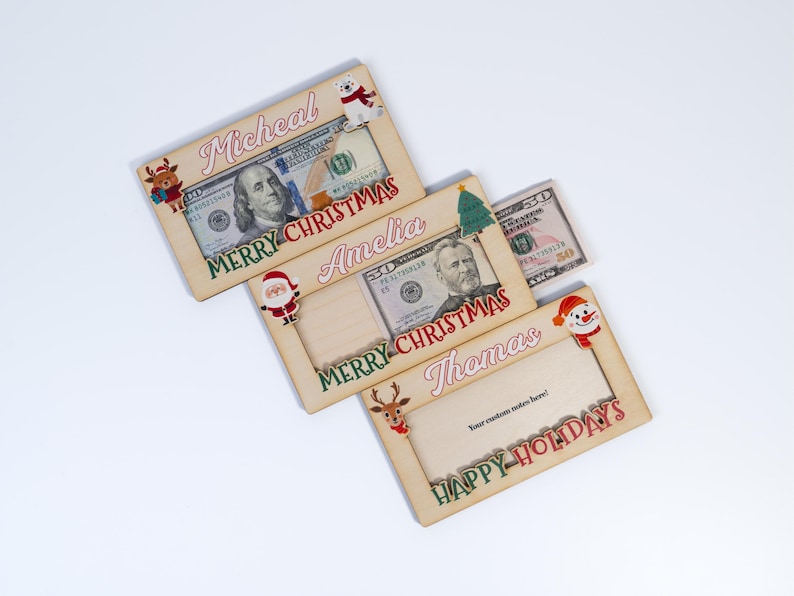 May include: Three wooden Christmas money holders with festive designs. The top holder says "Micheal Merry Christmas" and features a polar bear. The middle holder says "Amelia Merry Christmas" and features Santa Claus. The bottom holder says "Thomas Happy Holidays" and features a snowman.