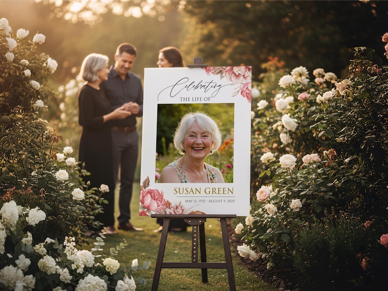 May include: A memorial sign on a wooden easel, featuring a photo of Susan Green, with the text "Celebrating the Life of Susan Green" and dates May 12, 1952 - August 9, 2023. The sign is decorated with pink and red floral accents.