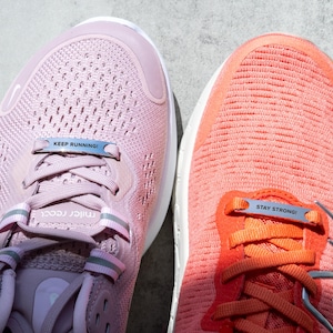 Puede incluir: Dos pares de zapatillas de running rosas y naranjas con cordones de metal plateado que tienen las palabras "Keep Running!" y "Stay Strong!"