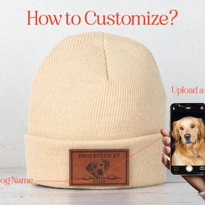 May include: A beige knitted beanie with a brown leather patch that says "Protected by" and has a space for a dog's name and picture. The text "Upload a picture" is visible above a smartphone displaying a golden retriever.