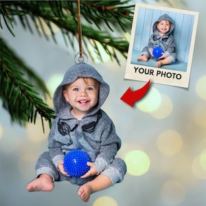 May include: A gray hooded ornament with a child wearing a gray hooded sweatshirt and holding a blue spiky ball. The ornament has a photo frame with the text "YOUR PHOTO" in the bottom right corner.