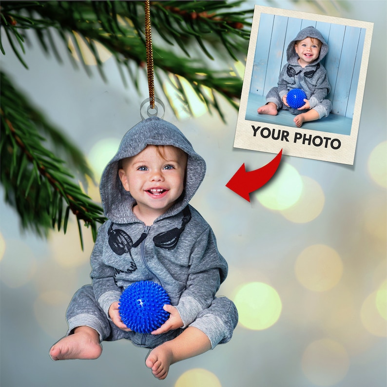 May include: A gray hooded ornament with a child wearing a gray hooded sweatshirt and holding a blue spiky ball. The ornament has a photo frame with the text "YOUR PHOTO" in the bottom right corner.