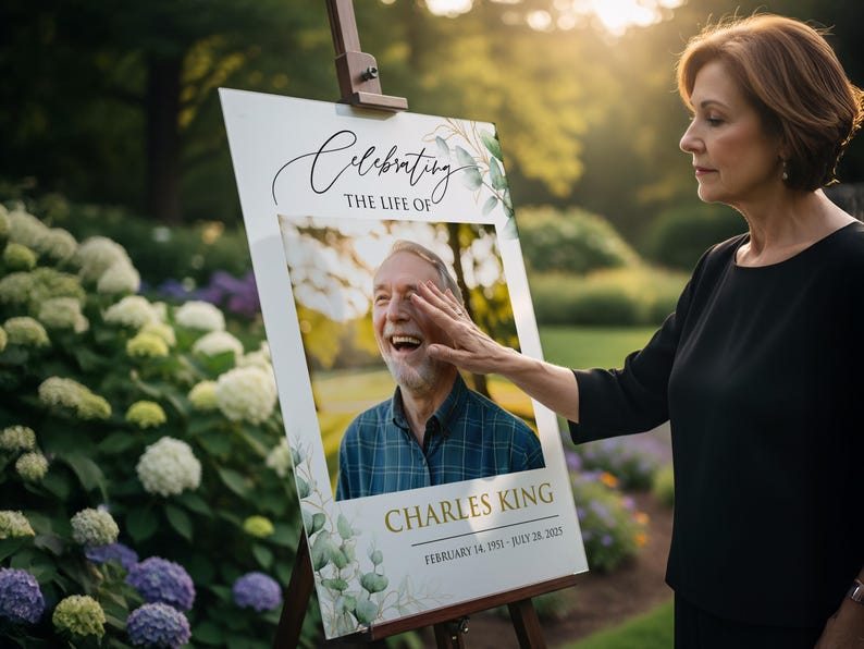 May include: A memorial sign on an easel with the text "Celebrating the Life of Charles King". The sign includes a photo of a smiling man and dates: February 14, 1951 - July 28, 2023. A woman touches the sign.