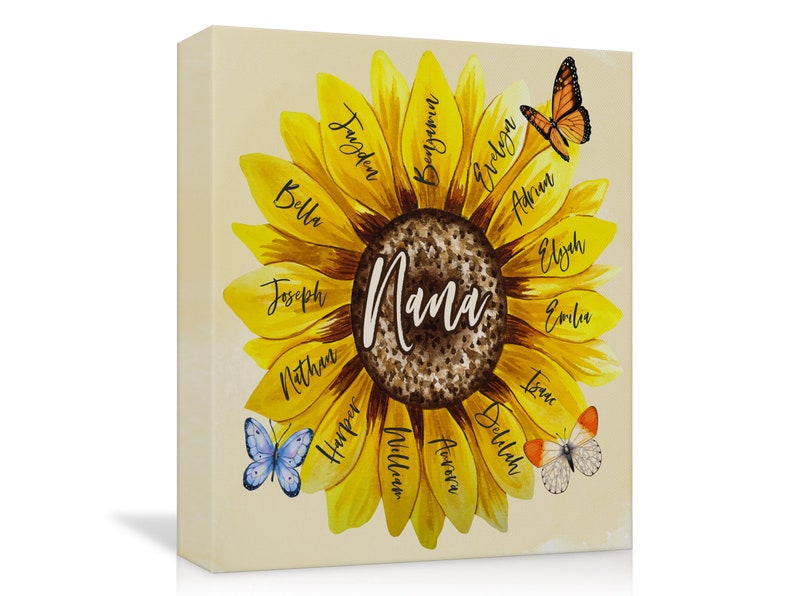 May include: A canvas print featuring a sunflower design with the word "Nana" in the center. The sunflower petals display names like Bella, Joseph, and Harper. Butterflies in orange and blue are scattered around the flower, creating a personalized and decorative piece.