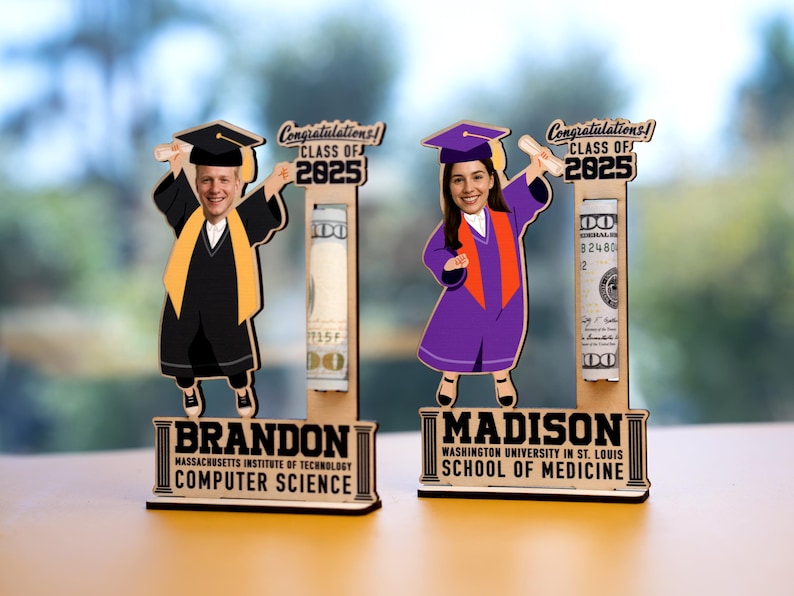 Op de afbeelding: Houten afstudeercadeau met cartoonfiguren in toga's en baretten, met diploma's. De figuren zijn gepersonaliseerd met namen en schoolinformatie. Elke figuur heeft een gleuf om opgerolde biljetten in te bewaren. Tekst: "Gefeliciteerd! Klas van 2025."