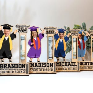 Op de afbeelding: Houten displays met een afstudeerthema met stripfiguren in afstudeerkleding, elk met een diploma. De displays bevatten de tekst "Gefeliciteerd! Klas van 2025" en gepersonaliseerde namen en diploma's. Elke display bevat een opgerolde bankbiljet.