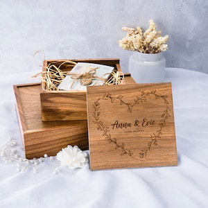 May include: A wooden box with a heart-shaped design engraved with the text "Anna & Eric June 18, 2023". The box is made of light brown wood and has a natural finish. The box is open and there is a smaller box inside.
