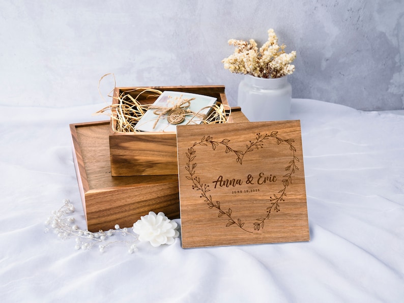 May include: A wooden box with a heart-shaped design engraved with the text "Anna & Eric June 18, 2023". The box is made of light brown wood and has a natural finish. The box is open and there is a smaller box inside.