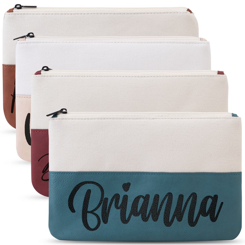 K&ouml;nnte beinhalten: Vier Rei&szlig;verschlusstaschen aus Canvas mit zweifarbigem Design. Der obere Teil ist aus wei&szlig;em Canvas und der untere Teil aus Kunstleder in einer anderen Farbe. Die unterste Tasche tr&auml;gt den Namen "Brianna" in schwarzer Schrift auf dem t&uuml;rkisfarbenen Kunstleder.