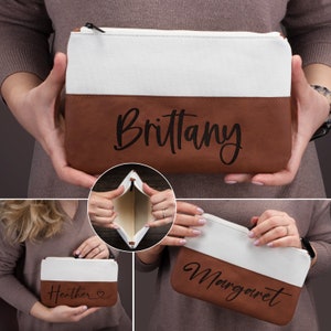 K&ouml;nnte beinhalten: Drei braune und wei&szlig;e Canvas-Rei&szlig;verschlusstaschen mit verschiedenen Namen, die auf den braunen Lederboden gestickt sind. Die Namen sind Brittany, Heather und Margaret.