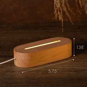 May include: A wooden LED light base, measuring 5.75 inches long and 1.38 inches high, with a warm, glowing light. The light is rectangular with rounded edges and a white power cord.