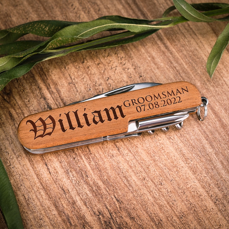 Może przedstawiać: Drewniany scyzoryk z personalizowanym grawerem, kt&oacute;ry brzmi "William Groomsman 07.08.2022".