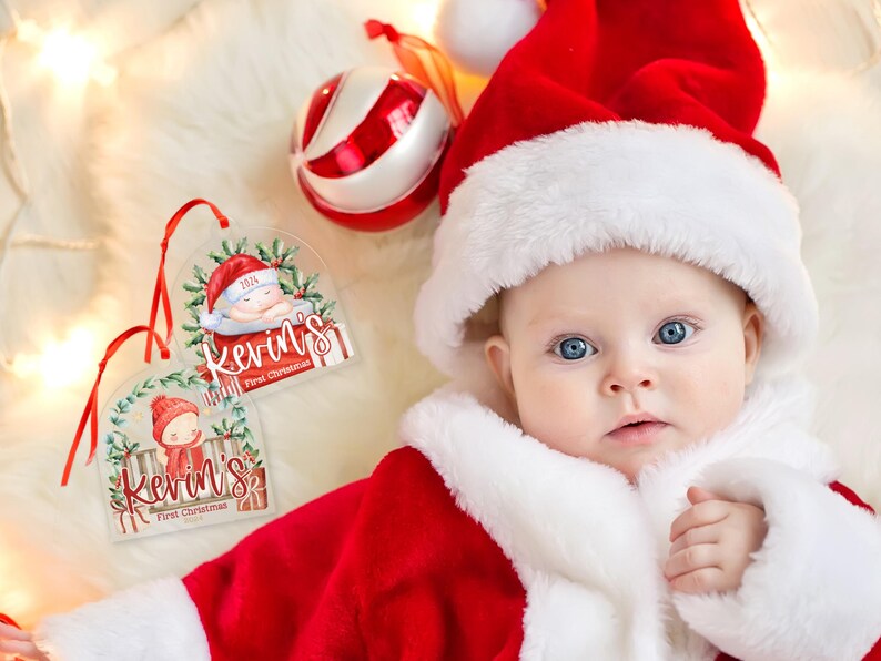 May include: Two clear acrylic Christmas ornaments featuring a watercolor illustration of a baby in a red hat, green holly, and the text Kevin's First Christmas 2024, each hanging from a thin red ribbon.