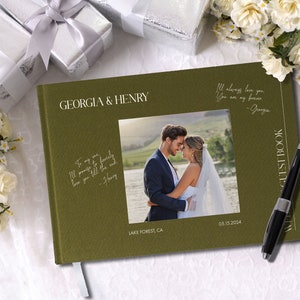 Puede incluir: Un libro de visitas de boda verde con los nombres "Georgia & Henry" en la portada. El libro tiene una foto de la pareja en la portada y el texto "Lake Forest, CA 05.15.2024". El texto "I'll always love you. You are my forever - Georgia" est&aacute; escrito en el lado derecho de la portada. Un bol&iacute;grafo negro est&aacute; sobre el libro.
