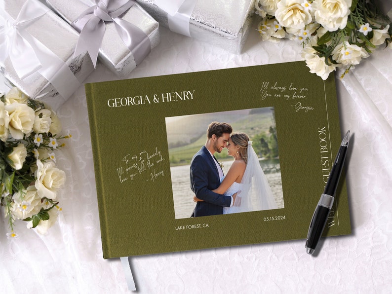Puede incluir: Un libro de visitas de boda verde con los nombres "Georgia & Henry" en la portada. El libro tiene una foto de la pareja en la portada y el texto "Lake Forest, CA 05.15.2024". El texto "I'll always love you. You are my forever - Georgia" est&aacute; escrito en el lado derecho de la portada. Un bol&iacute;grafo negro est&aacute; sobre el libro.