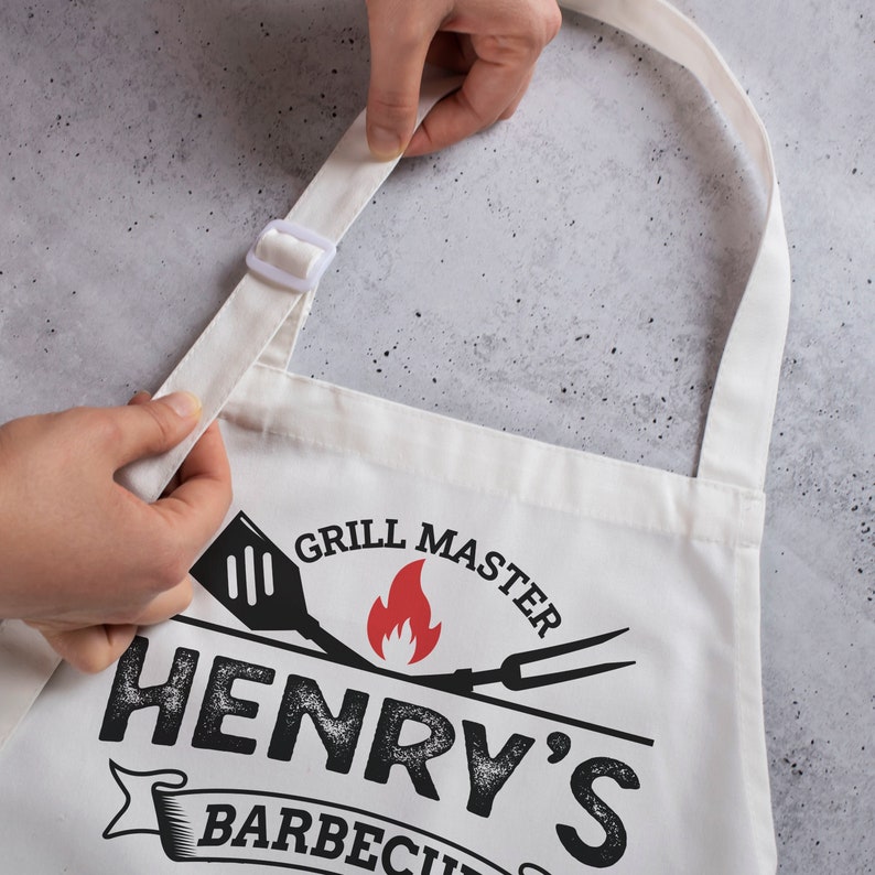 May include: White cotton apron with adjustable straps. The apron has a black and red design with the text "Grill Master Henry's Barbecue".