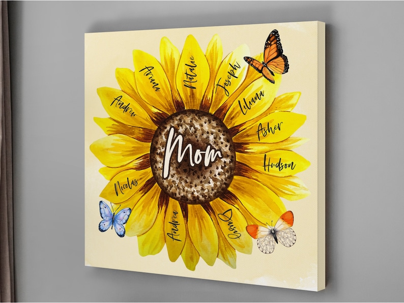May include: A canvas print featuring a sunflower design with the word "Mom" in the center. The sunflower petals display names in black script. Butterflies in shades of orange, blue, and white are scattered around the flower.