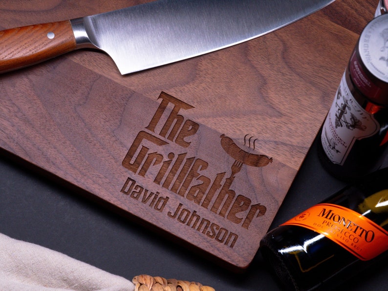 May include: A personalized walnut cutting board with the text "The Grillfather David Johnson" engraved on it. A knife and bottles of wine are also pictured.