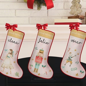 May include: Three personalized Christmas stockings with red trim and bows. Each stocking features a different illustration: a ballerina, a nutcracker, and a mouse with a sword. The names "Elena", "Felix", and "Oscar" are written on each stocking.