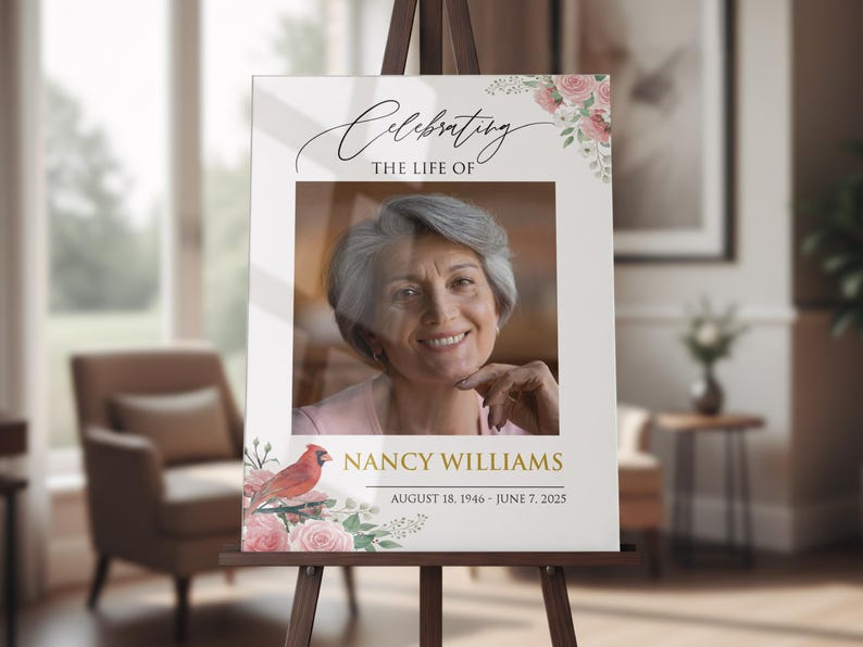 May include: A memorial sign on an easel, featuring a photo of a woman with gray hair. The sign reads "Celebrating the Life Of" and "Nancy Williams, August 18, 1946 - June 7, 2025." Floral and bird illustrations adorn the corners.