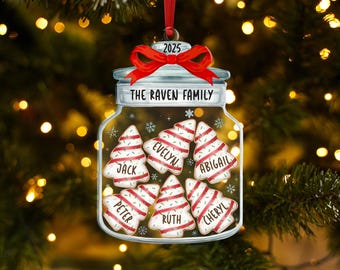 May include: A personalized Christmas ornament shaped like a jar, with a red bow and the year 2025. Inside are Christmas tree-shaped cookies with names: Jack, Evelyn, Abigail, Peter, Ruth, and Cheryl. The text "THE RAVEN FAMILY" is above the cookies.