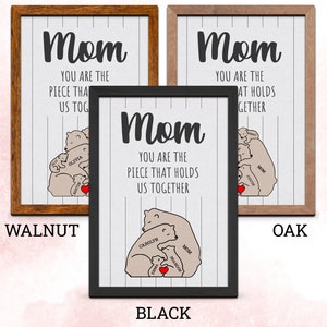 May include: A framed print with a white background and black text that reads "Mom you are the piece that holds us together". The print features a cartoon illustration of a mother bear hugging her cubs. The cubs are labeled with names. The frame is available in walnut, black, and oak.