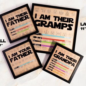 May include: Framed wooden art prints with black frames. The prints feature the phrases "I AM THEIR FATHER", "I AM THEIR GRAMPS", "I AM YOUR FATHER", and "I AM THEIR GRANDPA". Each print has a lightsaber design and names.