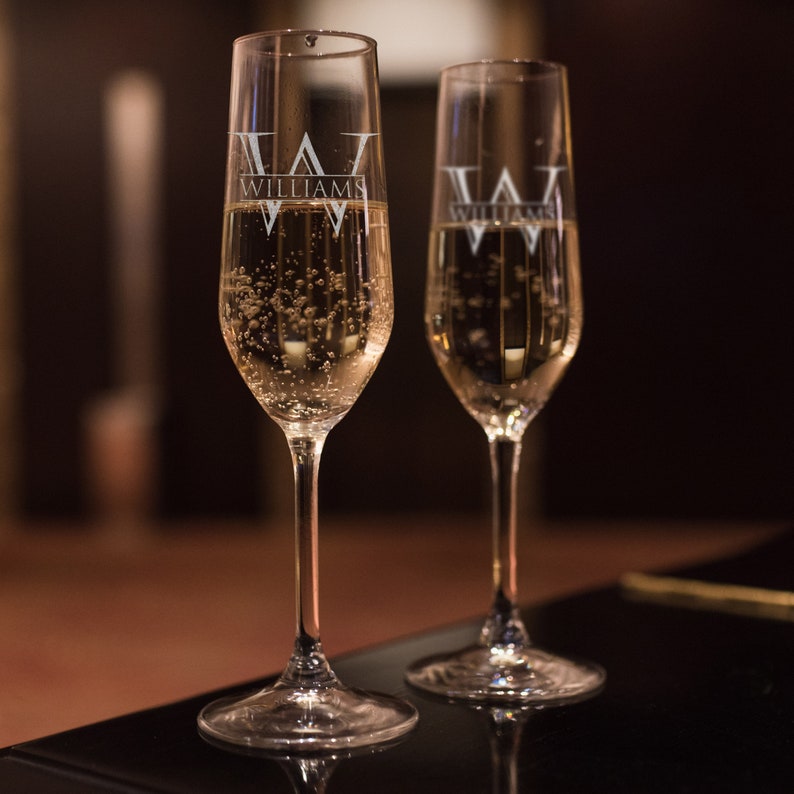 May include: Two clear champagne flutes filled with sparkling wine. The flutes are engraved with the text "Williams" and a stylised "W".