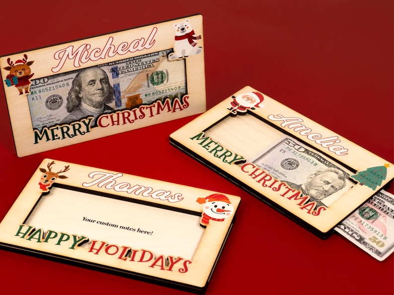 May include: Three wooden Christmas money holders with different designs. The first holder has a reindeer, the second has a snowman, and the third has a Santa Claus. Each holder has a slot for cash and a personalized name. The text on the holders reads "Micheal Merry Christmas", "Amelia Merry Christmas", and "Thomas Happy Holidays".