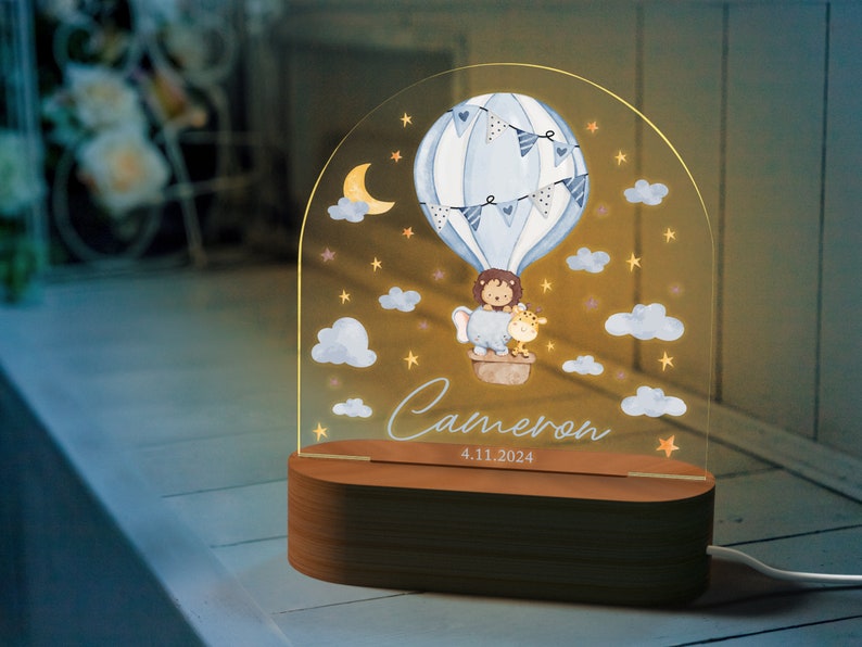 May include: A decorative night light featuring a watercolor illustration of a hot air balloon with a lion and giraffe. The light has a wooden base and the name "Cameron" and date "4.11.2024" are displayed.