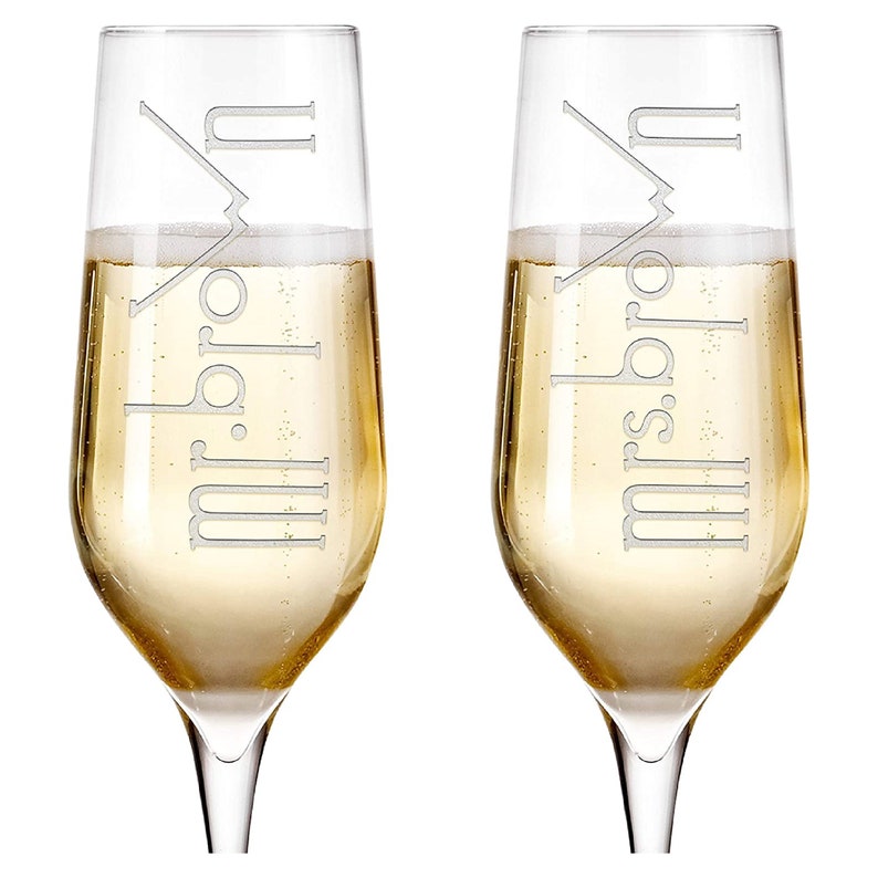 May include: Two champagne flutes with the words "Mr. & Mrs." etched on them. The flutes are filled with champagne.