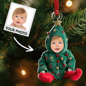 Pu&ograve; includere: Un ornamento natalizio a forma di bambino che indossa un costume da albero di Natale verde con stivali rossi. L'ornamento ha una stella dorata in cima e perline rosse e dorate per la decorazione. L'ornamento &egrave; appeso a un nastro rosso.