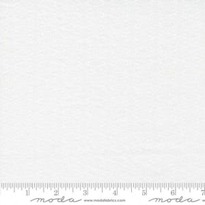 May include: A white fabric featuring a subtle, repeating geometric diamond pattern across the surface. A ruler is visible at the bottom edge, showing measurements in inches, with the text moda and www.modafabrics.com printed along the bottom.