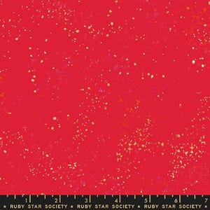May include: Red fabric with a speckled pattern. The fabric has small, irregular dots in shades of gold, pink, and orange scattered across the surface. The bottom of the image has a black ruler with the text "RUBY STAR SOCIETY".