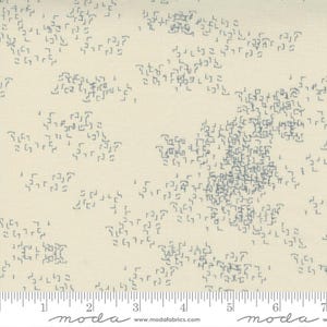 May include: A beige fabric with a repeating pattern of small, gray, geometric shapes. The fabric is measured with a ruler in inches.