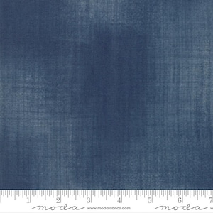 May include: Close-up of a textured, indigo blue fabric. The fabric has a subtle, mottled appearance with vertical and horizontal lines. The bottom of the image shows a ruler with inch markings and the word "moda" and the website address.
