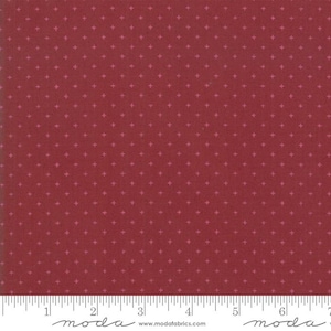 May include: A close-up of a fabric with a deep red background and a repeating pattern of small, light pink crosses. The fabric is marked with a ruler along the bottom edge. The word "moda" is printed at the bottom.