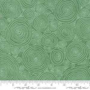 May include: Green fabric with a repeating pattern of white concentric circles and geometric shapes. The fabric has a textured appearance and a ruler is at the bottom. The word "moda" and website address are printed at the bottom.
