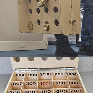 May include: A wooden game with a frog-shaped handle and a series of holes. The game has a drawer with compartments labeled with different point values, including 100, 900, 2000, 4000, 500, 600, 700, 800, and 1000.